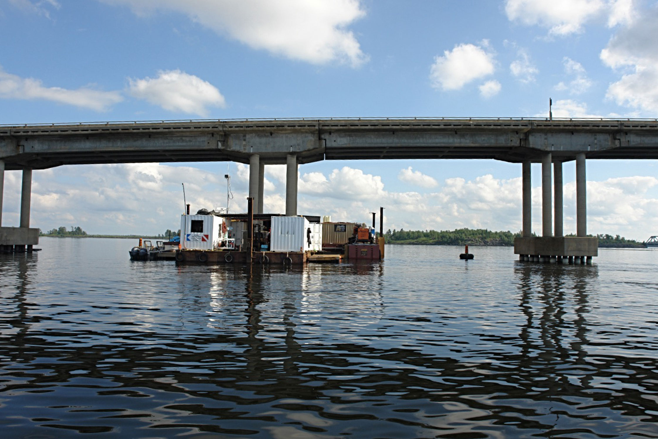 A barge assembly surrounding one of three in-water, concrete girder structures under the Noden Causeway Bridge.
